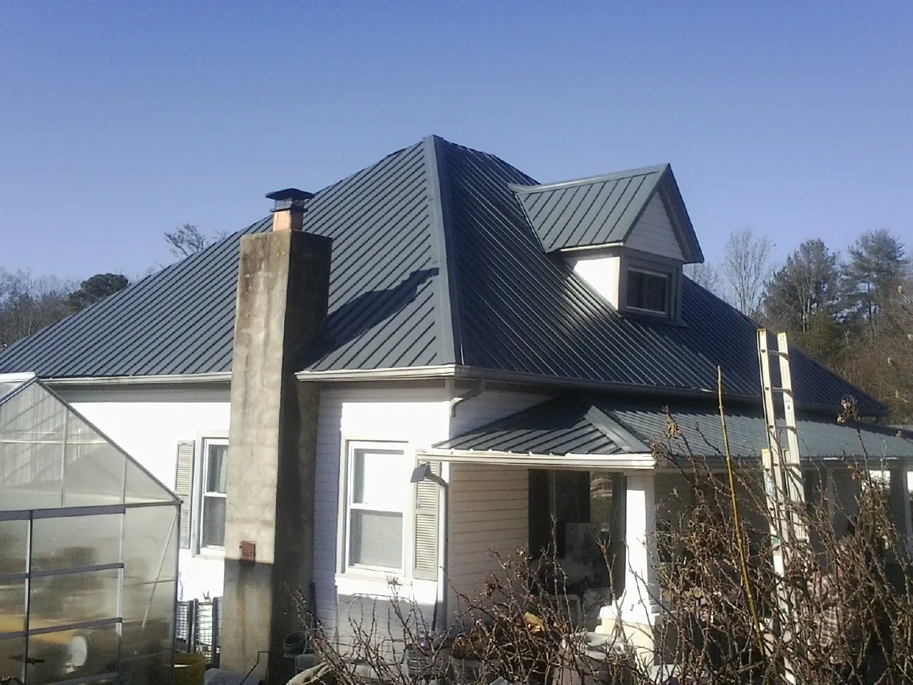 Dark blue standing seam metal roof on a white farmhouse with dormer — Slate & Tile Roof Repair by Roofing Brothers in Lake Huntington