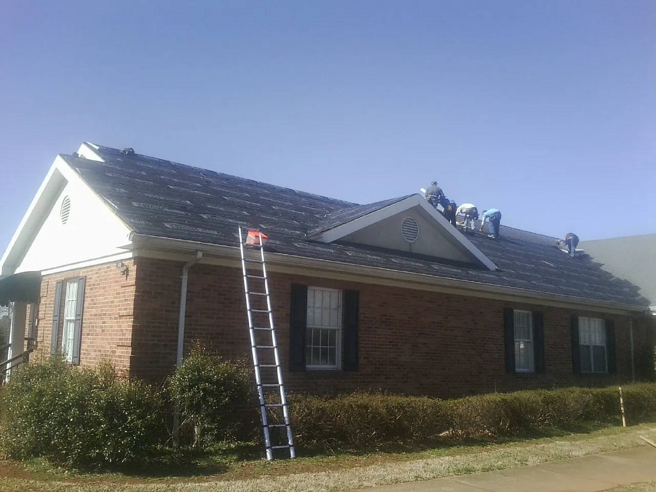 Crew tearing shingles off a brick ranch roof with a ladder set — Emergency Roof Repair work by our crew in Lake Huntington