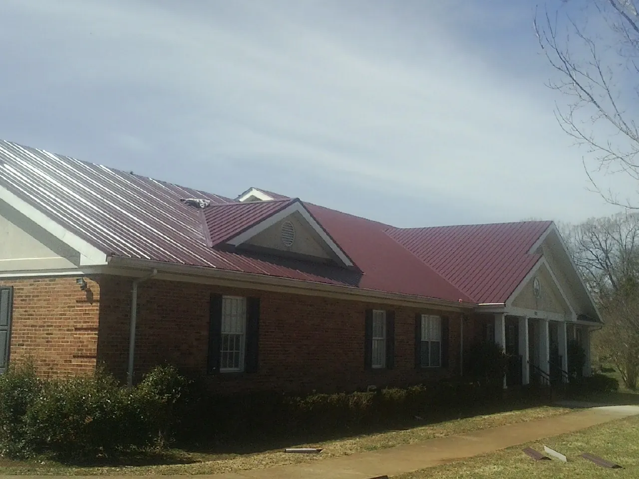 Red metal roof with gabled entries on a long brick building, from a Hail Damage Roof Repair job in Lake Huntington