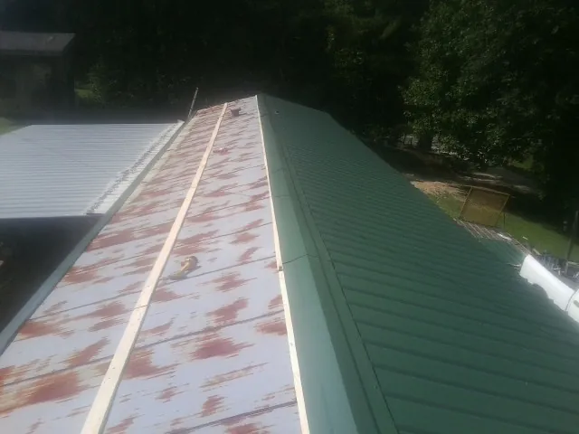 Old rusted panels beside newly installed green metal roofing — Wind Damage Roof Repair by Roofing Brothers in Lake Huntington