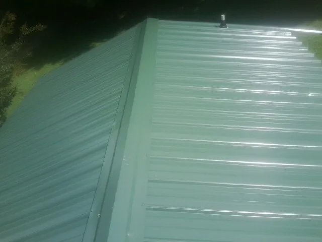 New green metal panels meeting at the ridge of a roof — Flat Roof Repair work by our crew in Lake Huntington