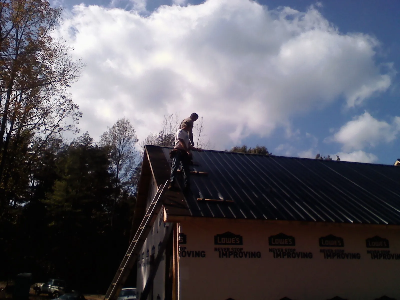 Roofer fastening dark metal panels high against a cloudy sky, from a Roof Inspection job in Lake Huntington