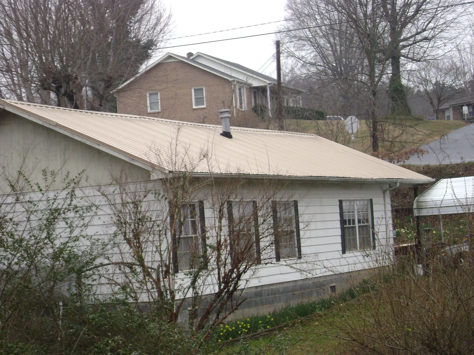 Tan metal roof on a white sided house set into a hillside — Commercial Roofing by Roofing Brothers in Lake Huntington